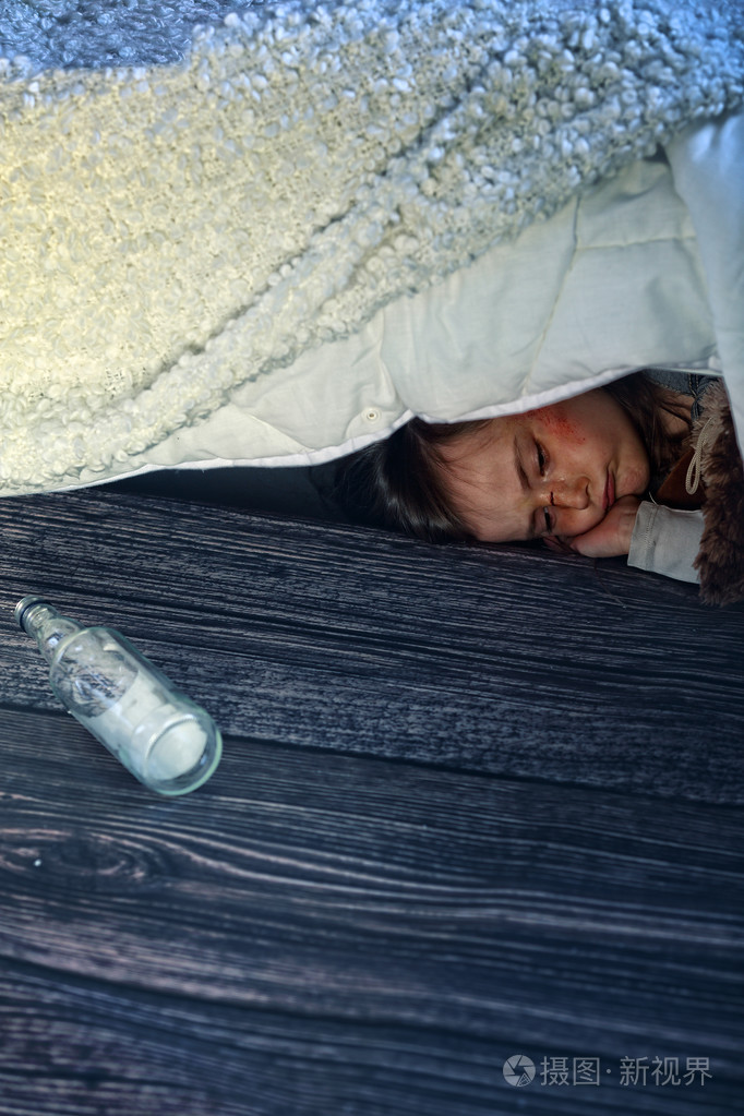 在酒精的家人害怕的女孩躲在床底下