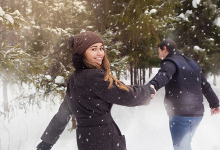 爱在冬季公园散步的年轻夫妇。它正在下雪，冬天