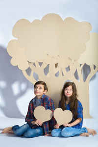 男孩和女孩保持心坐树下纸板。爱情观