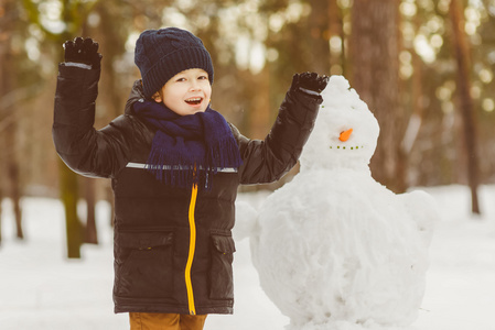 冬季活动的概念。快乐的小男孩制作雪人户外