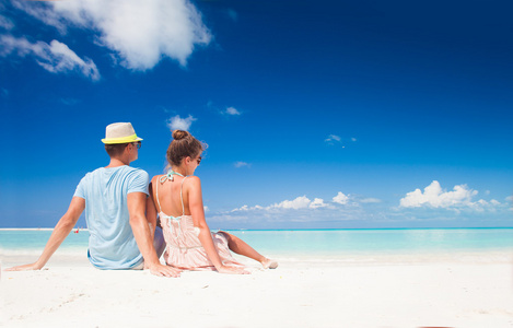后视图在明亮的衣服和帽子坐在热带海滩夫妇