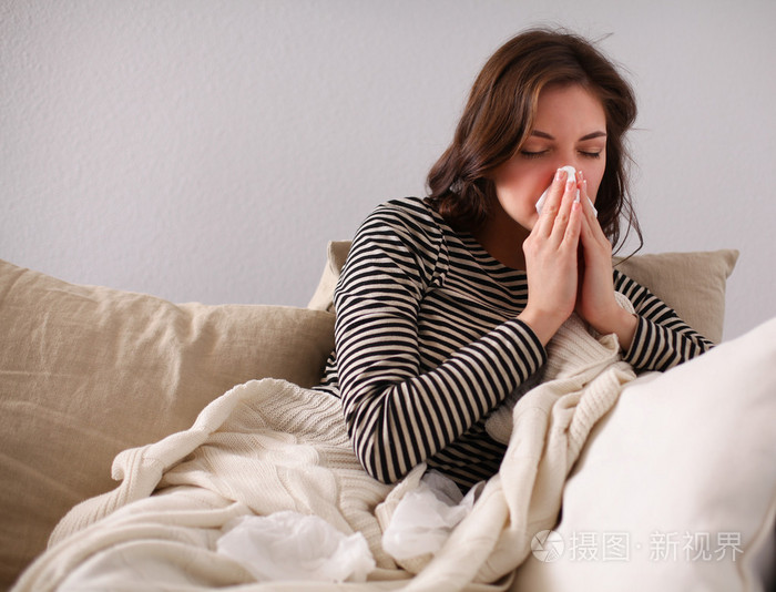 一个生病的女人坐在沙发上吹她的鼻子的肖像