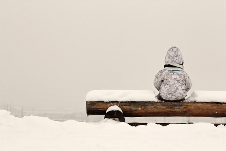 孩子坐在长椅上满了雪