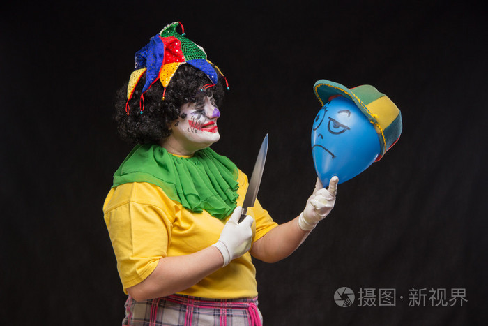 生气的丑陋小丑想要杀死一个戴着帽子的气球照片-正版商用图片1lu5ph