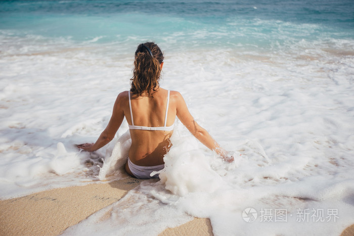 坐在白色的沙滩泳装的年轻女子的背影