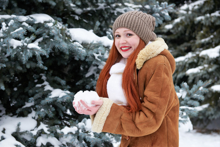 女人在冬季公园的少数雪看天。与雪杉树