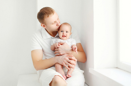 快乐年轻父亲抱着婴儿在家里窗户附近的白色房间