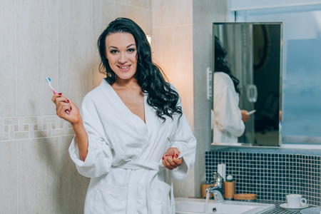 有魅力的女人在浴室一件白色外套刷牙的画像。健康的牙齿