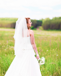 美丽的新娘与户外中字段的婚礼花束