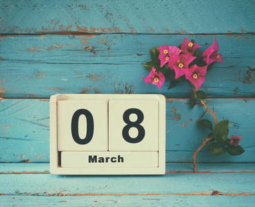 木制的 3 月 8 日日历，旁边旧蓝色仿古桌上紫色的花。选择性的焦点