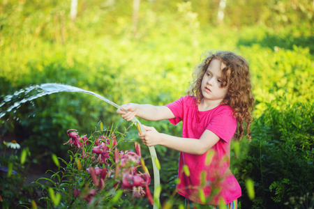 在晴朗的一天浇水花在花园园艺的小女孩照片