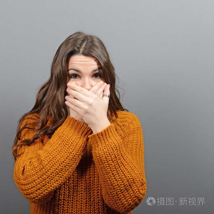 捂着嘴用手在灰色背景下的女人