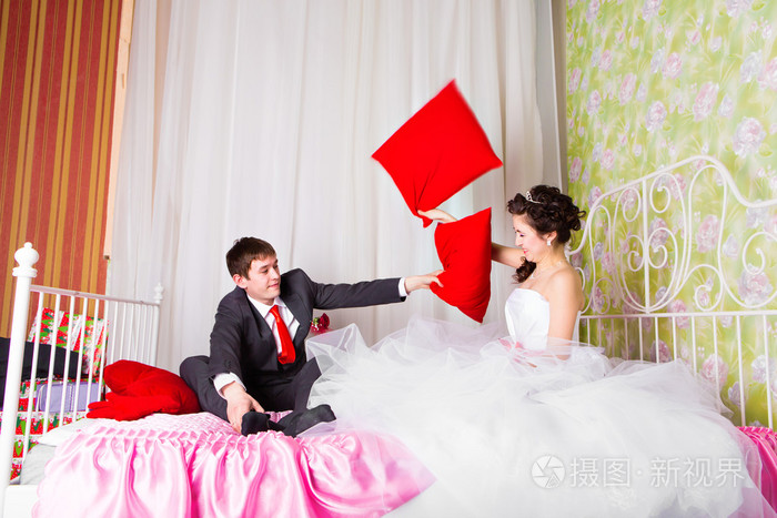 幸福的新婚夫妇和枕头在床上打架的肖像