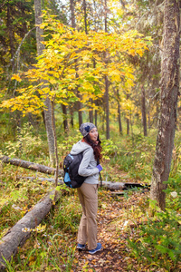走在秋天的树林的背包徒步旅行者年轻女子
