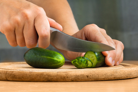 妇女的手切片黄瓜在切菜板上