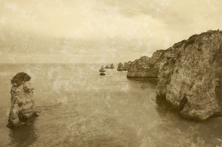 美丽的岩层，石拱门和洞在多纳安娜海滩和帆船在傍晚的光线 拉各斯，阿尔加维海岸，葡萄牙 地平线上。复古老年棕褐色照片与划痕