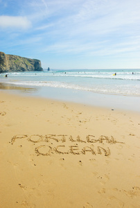单词葡萄牙和海洋都写在葡萄牙阿尔加维地区风景秀丽的海滩上。人们游泳和冲浪。岁的照片。黑色和白色