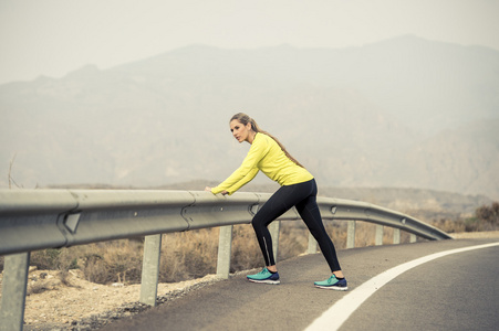 沥青路面与干燥的沙漠地貌在硬健身培训会话中运行锻炼后拉伸腿部肌肉的运动女人