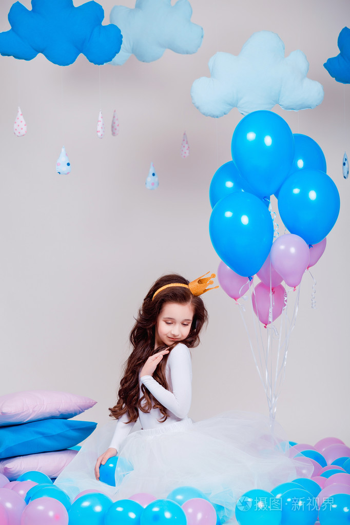 照片 可爱的小公主女孩坐在房间里的气球在白色背景.看着照相机.童年.