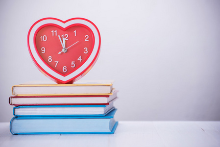 红色的心时钟和堆栈的木制的桌子上的书