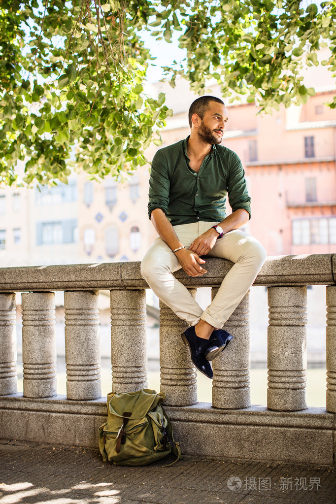 侧面图的坐在树下的篱笆上有胡子的人