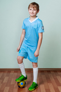 穿着足球制服的小男孩一条腿站在球上
