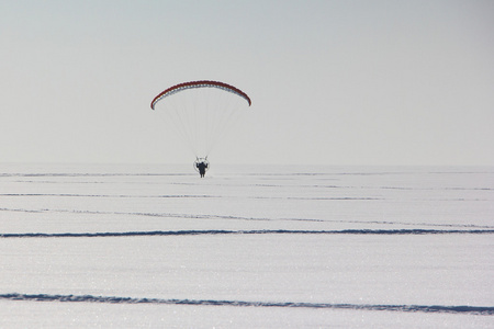 在白雪的衬托下的机动 paraplane 飞的人