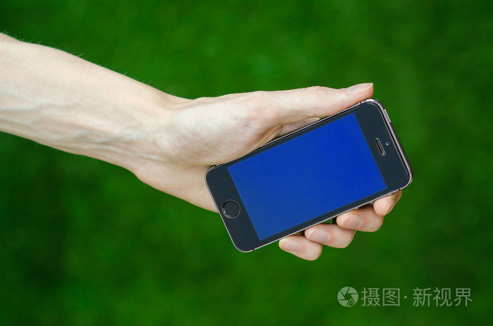 人的手,握著现代手机与一个蓝色屏幕上绿草第一人称视图的背景
