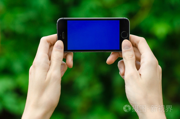 人的手握著现代手机与一个蓝色屏幕上绿草第一人称视图的背景
