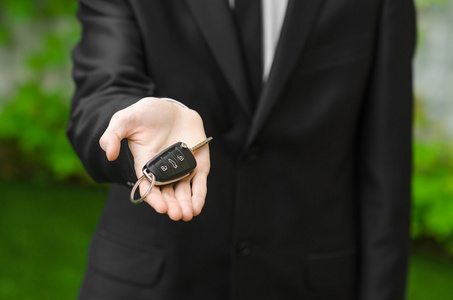 新车和商业主题 穿着黑色西装的男人拥有一辆新车的钥匙上绿草背景
