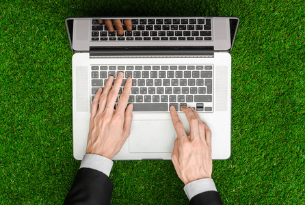 工作在户外和商人主题 人类的手在一套黑色西装和打开笔记本上的绿草顶视图的背景中显示手势