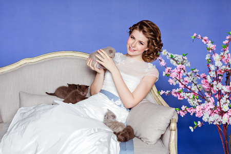 在坐在沙发上与樱花花，蓝色背景上的白色礼服微笑着对他五只小猫迷人和美丽的女孩