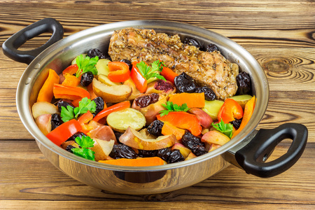 健康的食物，炖猪肉与各种五颜六色的蔬菜，在木制的背景上的平底锅