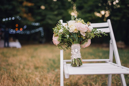 婚礼花束的牡丹鲜花和绿叶站在背景上的老式凳子和散景灯