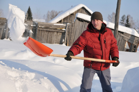 一个穿着红色外套，把红色的铲子干净的雪，在村里的街道上