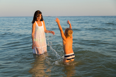 年轻的母亲和儿子在海里玩。一个美丽的年轻母亲和小男孩在水中快乐的游戏。海上的家庭假期。家庭和社会杂志 海报和网站的照片