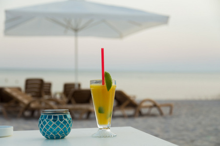 一杯在白桌上的果汁。在海滩上放松一下。美味的提神饮料。美丽的海景。图片为旅行和社会杂志海报背景和网站