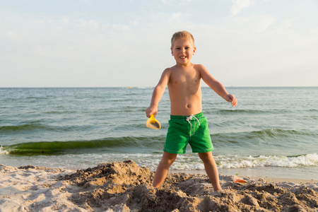 在海滩上的小男孩短裤。孩子们玩海砂。喜悦和孩子们的乐趣。一个美丽温暖的日子。儿童杂志和网站的照片