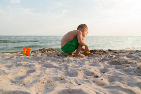 在海滩上的小男孩短裤。孩子们玩海砂。喜悦和孩子们的乐趣。一个美丽温暖的日子。儿童杂志和网站的照片