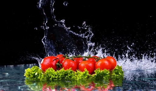 新鲜的番茄樱桃和绿色新鲜沙拉配水下降溅上深色背景宏的水滴落在红色的樱桃西红柿和轰动