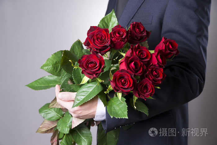 在灰色的背景上红玫瑰花束的男人