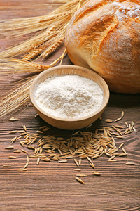 新鲜出炉的面包，一碗面粉和小麦耳朵上的木制的背景