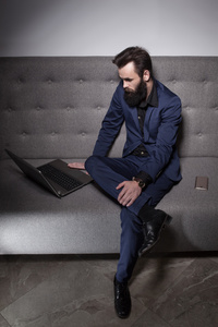 有胡子的人穿着西装，带着笔记本电脑浏览互联网