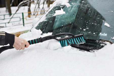 男人用刷子把汽车从雪上擦下来