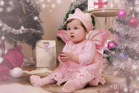 抱着粉红色蝴蝶翅膀的女婴坐在圣诞树下