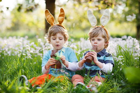 两个小男孩戴着复活节兔子耳朵，吃着巧克力