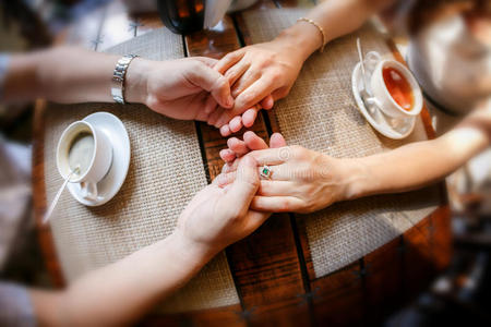 男人的手和女孩的手在一张桌子上，有一杯茶和一杯咖啡
