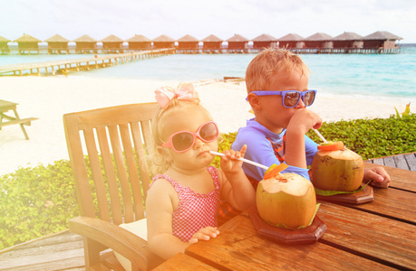 小男孩和蹒跚学步的女孩喝椰子鸡尾酒在海滩上