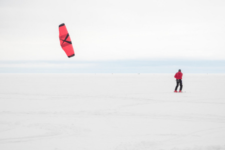 人在滑雪板上滑行，在白雪覆盖的湖面上放风筝。