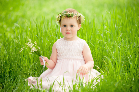 坐在户外的绿草上的花花环甜美女孩